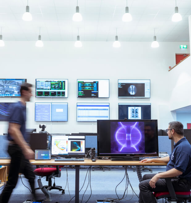 Fusion researcher inside control room looking at plasma on screen